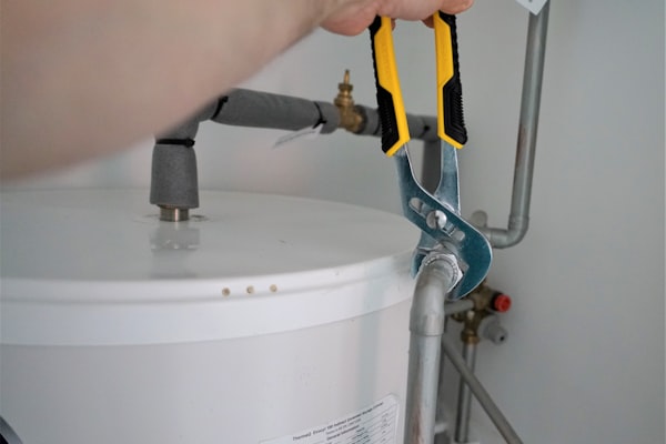 Professional plumber using wrench to service a water heater tank